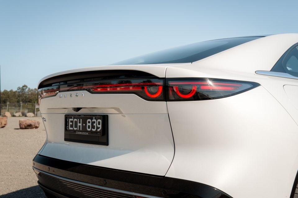 A close-up of the rear taillight and boot lid of a white 2027 Mazda 6e Atenza sedan, showing its illuminated red taillights and badge.