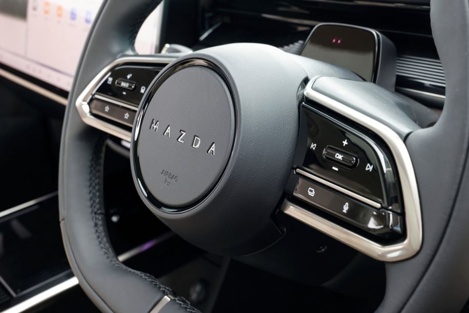 Close-up of the steering wheel controls and Mazda badge inside a 2027 Mazda CX-6e