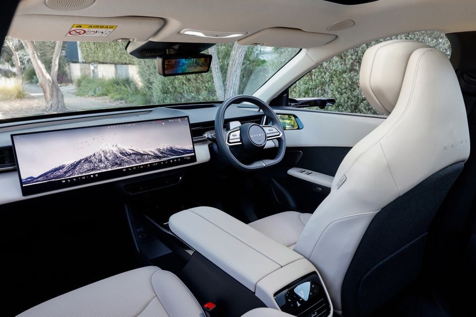 The interior of a 2027 Mazda CX-6e SUV, showing the dashboard, steering wheel, widescreen display and cream leather front seats.