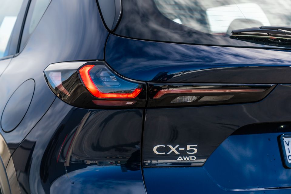 Close-up of the rear of a dark blue Mazda CX-5 AWD SUV, showing the tail light and model badge
