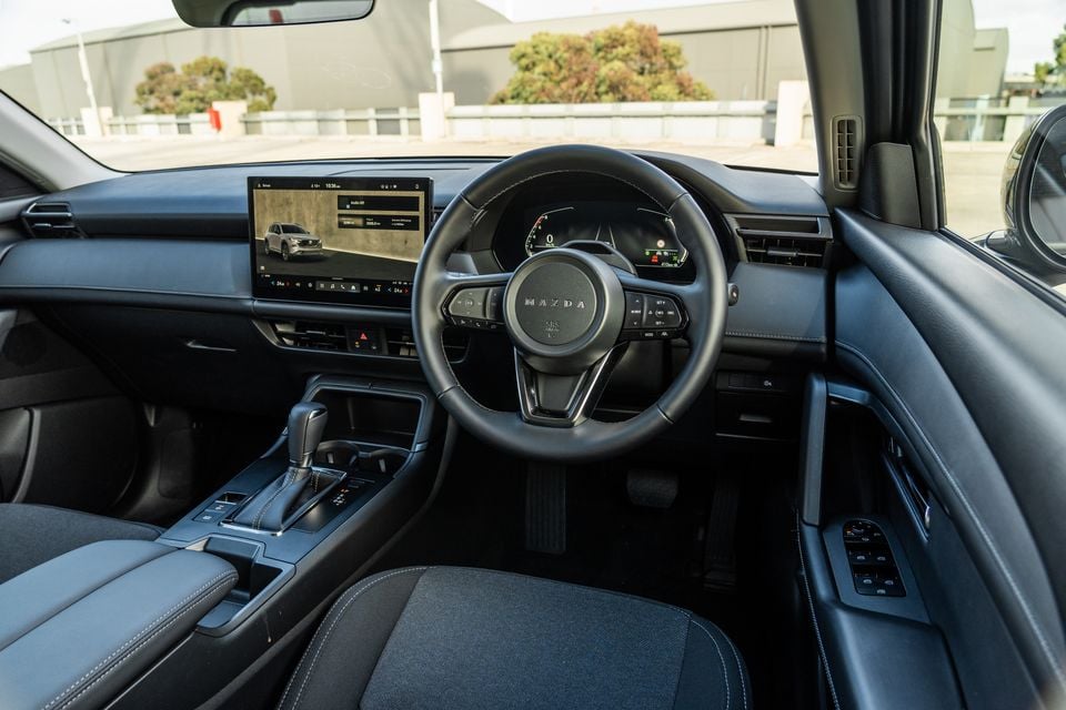 Interior of a Mazda CX-5 showing the dashboard, Mazda-branded steering wheel, touchscreen infotainment display, digital instrument cluster, and centre console with gear shifter