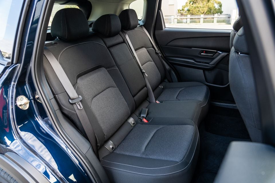Rear seats of a 2027 Mazda CX-5 showing black fabric upholstery with white contrast stitching and seatbelts, viewed through an open rear door