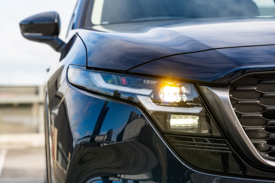 Close-up of the front headlight and grille on a dark blue Mazda CX-5, with the indicator light illuminated.
