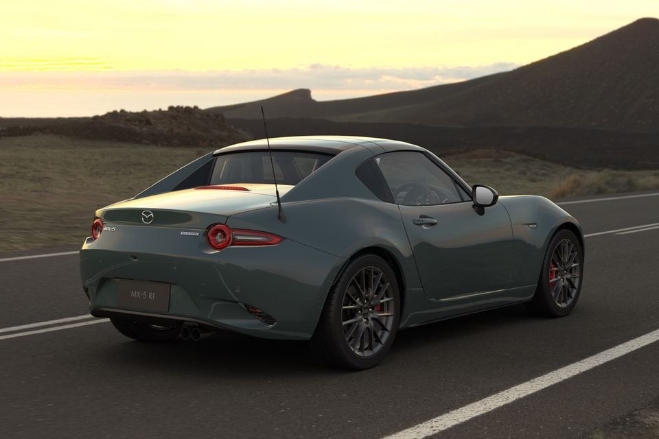 A grey-green 2027 Mazda MX-5 RF GT RS with a targa roof seen from the rear on a coastal road at sunset