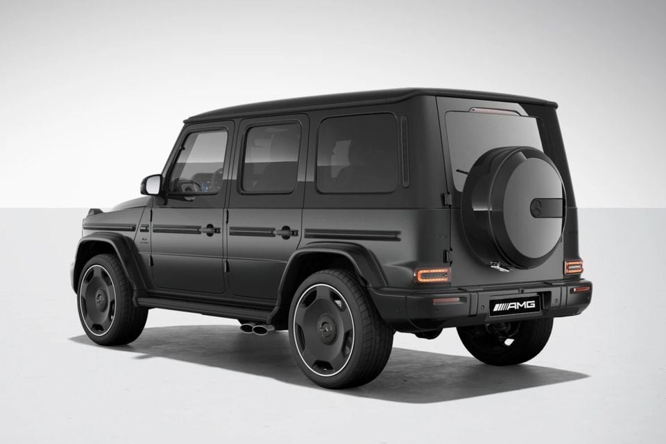 A dark grey Mercedes-AMG G63 SUV seen from the rear three-quarter angle, showing the spare wheel mounted on the rear door and AMG badging, against a studio background.