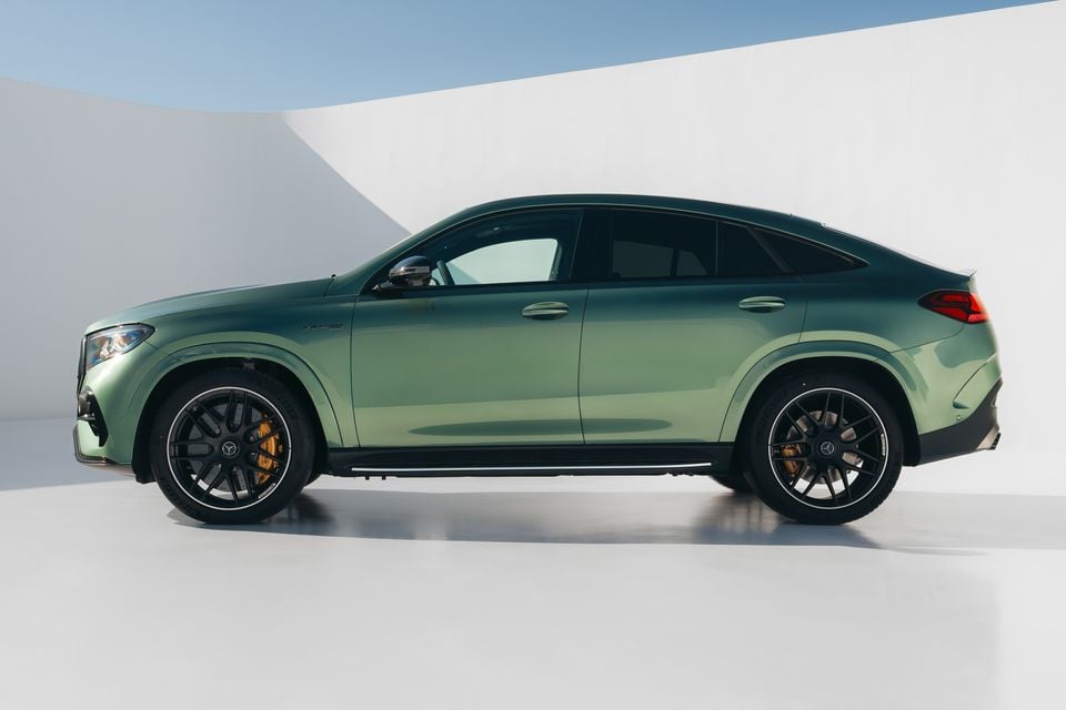 A green Mercedes-AMG GLE 63 S Coupe SUV seen from the side in a studio setting, featuring black multi-spoke wheels with gold brake calipers