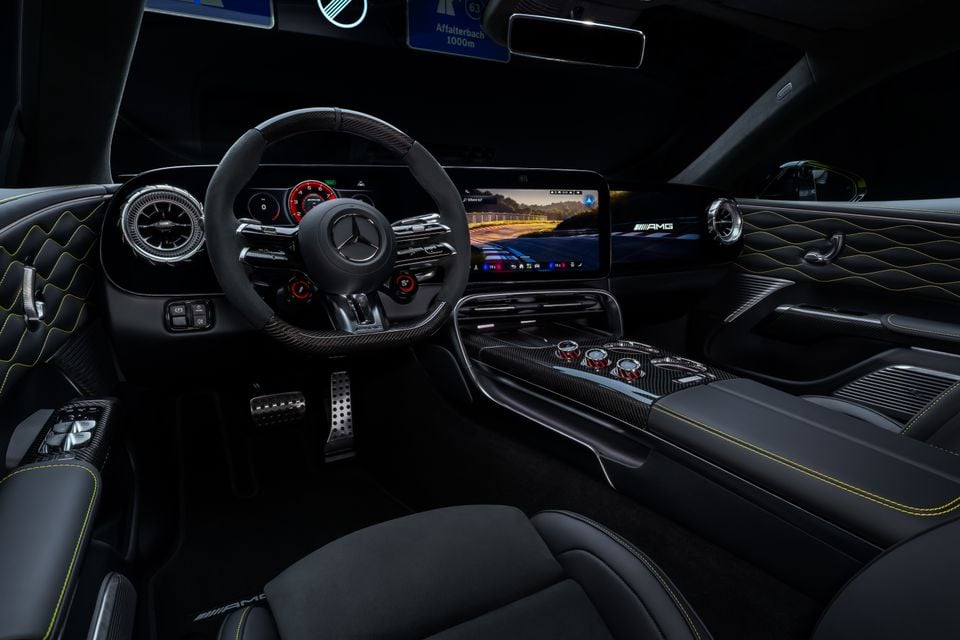 Interior of a Mercedes-AMG GT 4-Door Coupe showing the flat-bottomed steering wheel, digital instrument cluster, large central touchscreen, carbon fibre centre console, and black leather seats with yellow contrast stitching