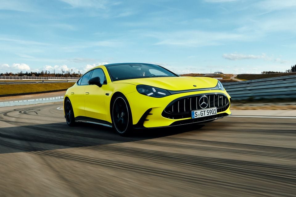 A yellow 2027 Mercedes-AMG GT 4-Door Coupe driving on a race track, seen from the front and side