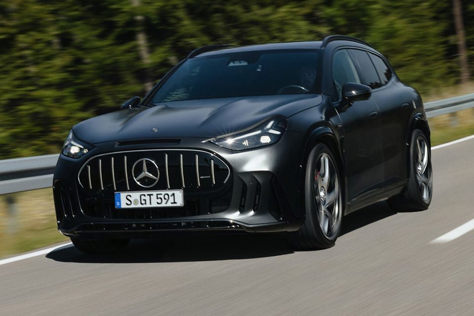 A black 2027 Mercedes-AMG GT SUV driving on a country road, seen from the front with its Panamericana grille