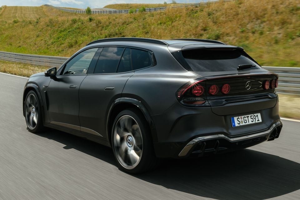 A dark grey 2027 Mercedes-AMG GT SUV driving on a test track, seen from the rear and side