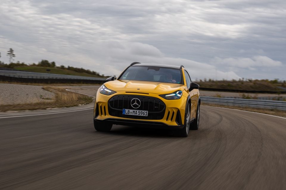 A yellow 2027 Mercedes-AMG GT 63 SUV driving around a curve on a race track, seen from the front