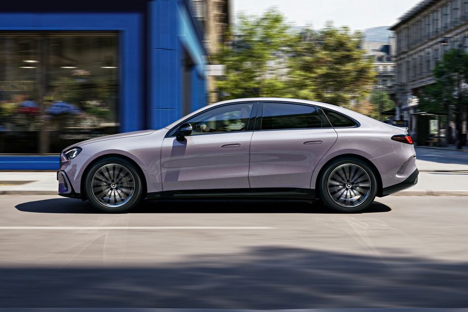 Um sedã elétrico Mercedes-Benz Classe C 2027 lilás prateado dirigindo por uma rua da cidade, visto de lado