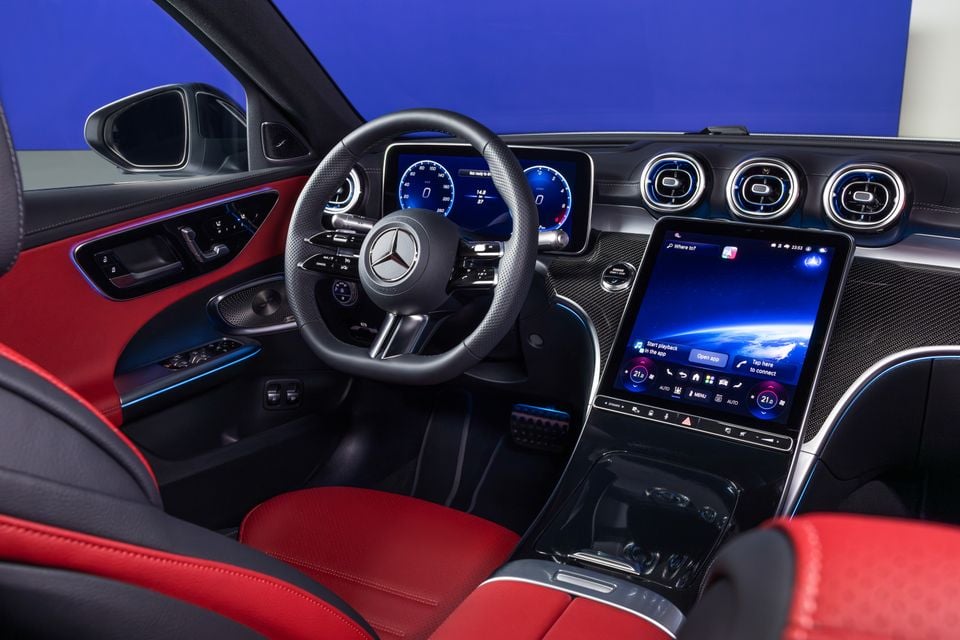 Interior of the 2027 Mercedes-Benz C-Class facelift showing the steering wheel, digital instrument cluster, large portrait infotainment touchscreen, and red and black upholstery