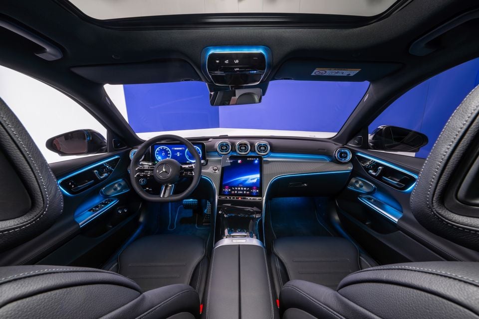 Interior of a 2027 Mercedes-Benz C-Class facelift showing the dashboard, steering wheel, large central touchscreen, and blue ambient lighting