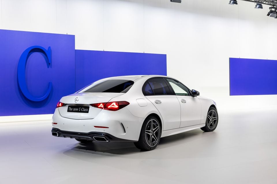 White Mercedes-Benz C-Class sedan seen from the rear three-quarter angle at an indoor brand reveal event