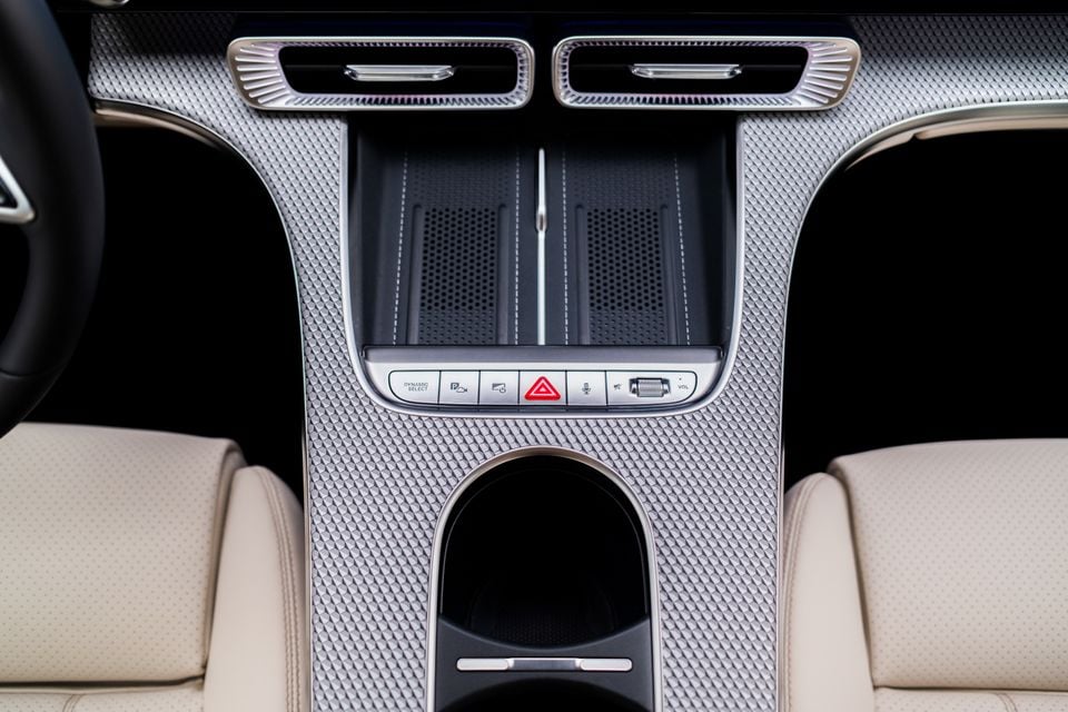 Interior centre console of the 2027 Mercedes-Benz C-Class electric, showing a textured silver panel with control buttons including Dynamic Select, hazard lights, and a volume dial, flanked by cream leather seats.