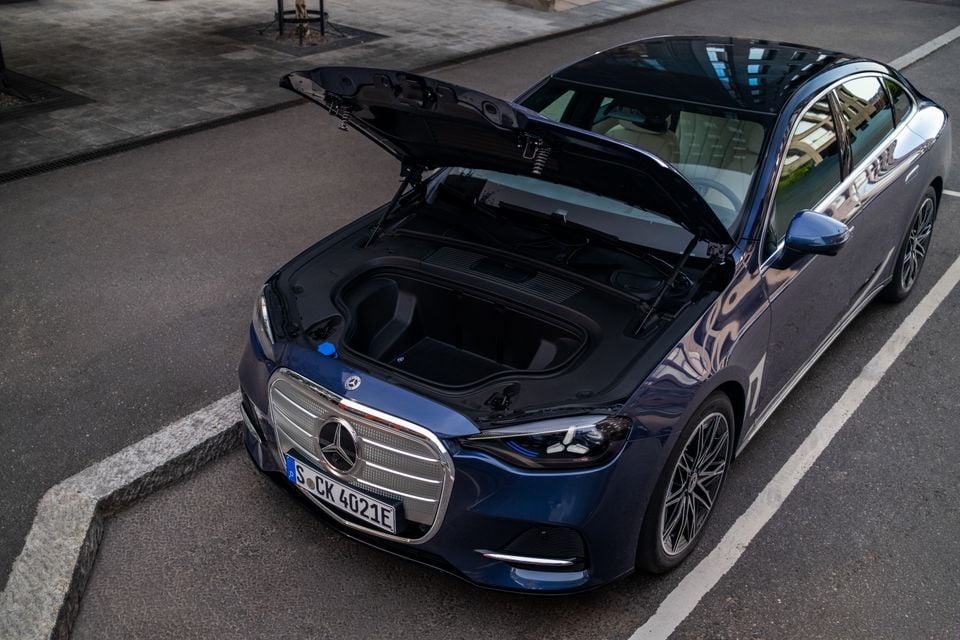 A dark blue Mercedes-Benz C-Class electric sedan with its front bonnet open, revealing the frunk storage compartment, seen from above and slightly to the front