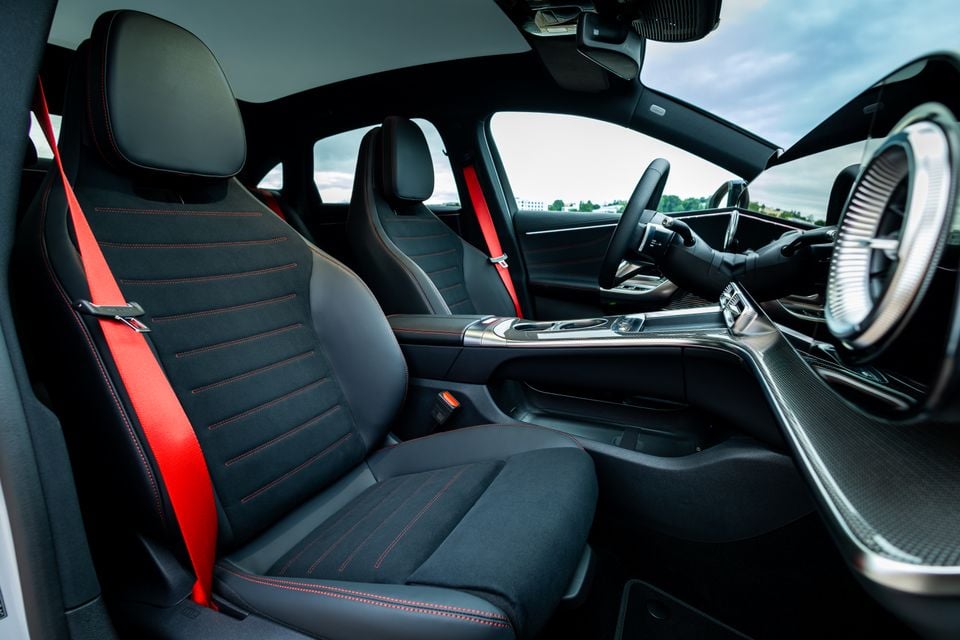 Interior view of a 2027 Mercedes-Benz C-Class electric showing black front seats with red stitching and red side bolsters, centre console, steering wheel, and carbon fibre-look trim