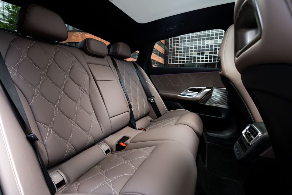 Rear interior of the 2027 Mercedes-Benz C-Class electric showing quilted tan leather rear seats with diamond stitching, seatbelts, and rear door controls