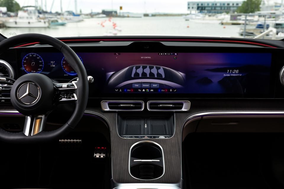 Interior dashboard view of a Mercedes-Benz C-Class Electric showing the large widescreen display with Sky Control ambient lighting settings, digital instrument cluster, steering wheel, and wood-trimmed centre console near a marina