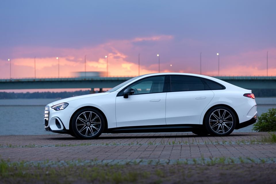 A white Mercedes-Benz C-Class electric fastback sedan parked beside a waterway at sunset, seen from the side