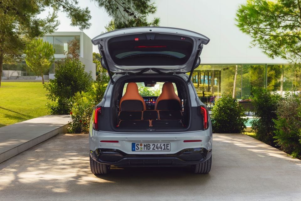 Rear view of a silver 2027 Mercedes-Benz GLB SUV with the tailgate open, revealing the boot and tan leather interior seats, parked in front of a modern home.