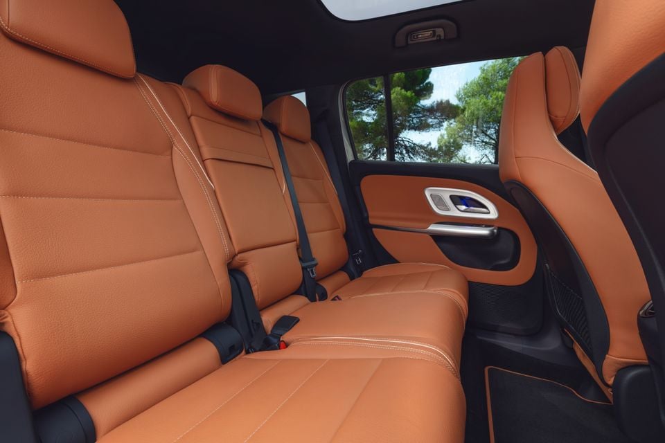 Tan leather rear seats of a Mercedes-Benz GLB, showing three-across seating with seatbelts and a door panel with window controls visible