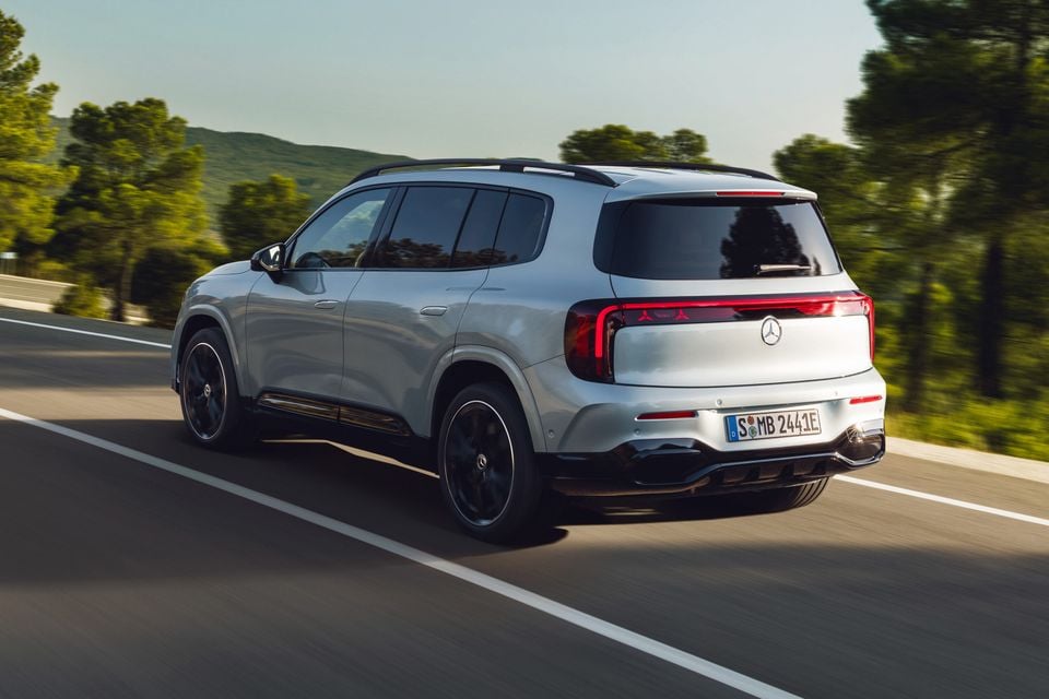 A silver 2027 Mercedes-Benz GLB SUV seen from the rear three-quarter angle while driving on a road lined with trees