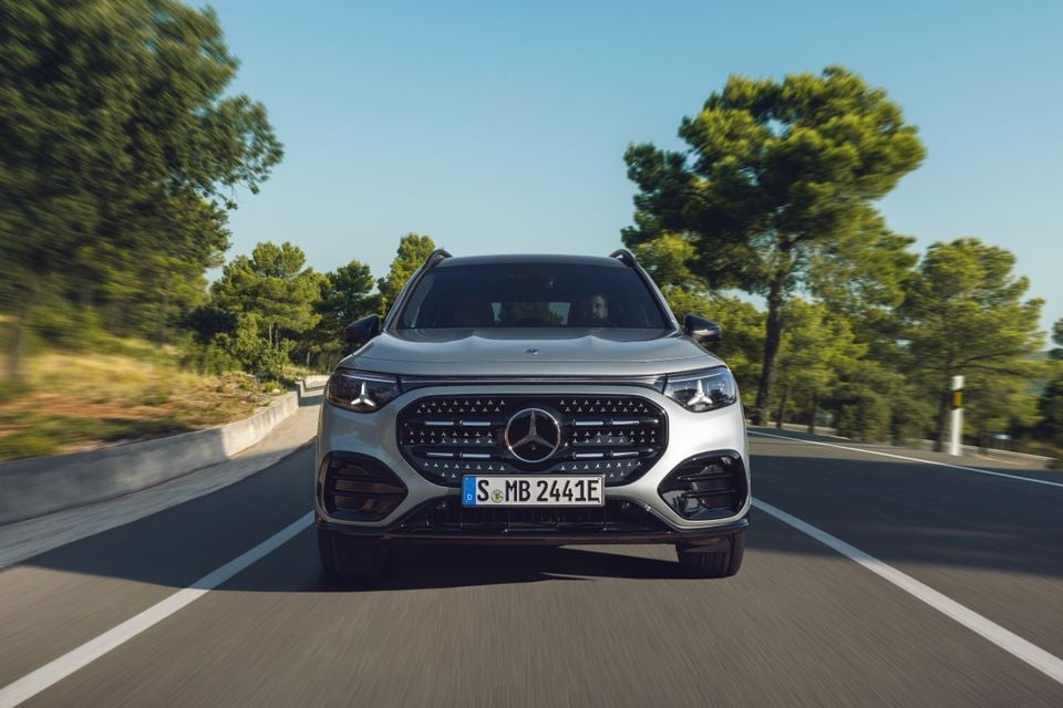 A silver Mercedes-Benz GLB SUV seen from the front while driving on a tree-lined road