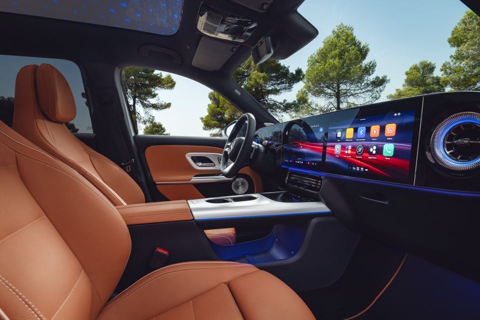 Interior of a Mercedes-Benz GLB showing tan leather seats, a large widescreen infotainment display with app icons, and ambient blue lighting