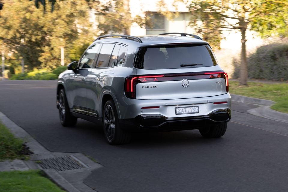 A silver 2027 Mercedes-Benz GLB 350 4Matic electric SUV driving along a suburban street, seen from the rear