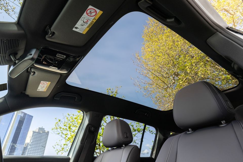 Panoramic glass sunroof in the 2027 Mercedes-Benz GLB 350 4Matic electric, viewed from inside with dark leather front seats and trees overhead