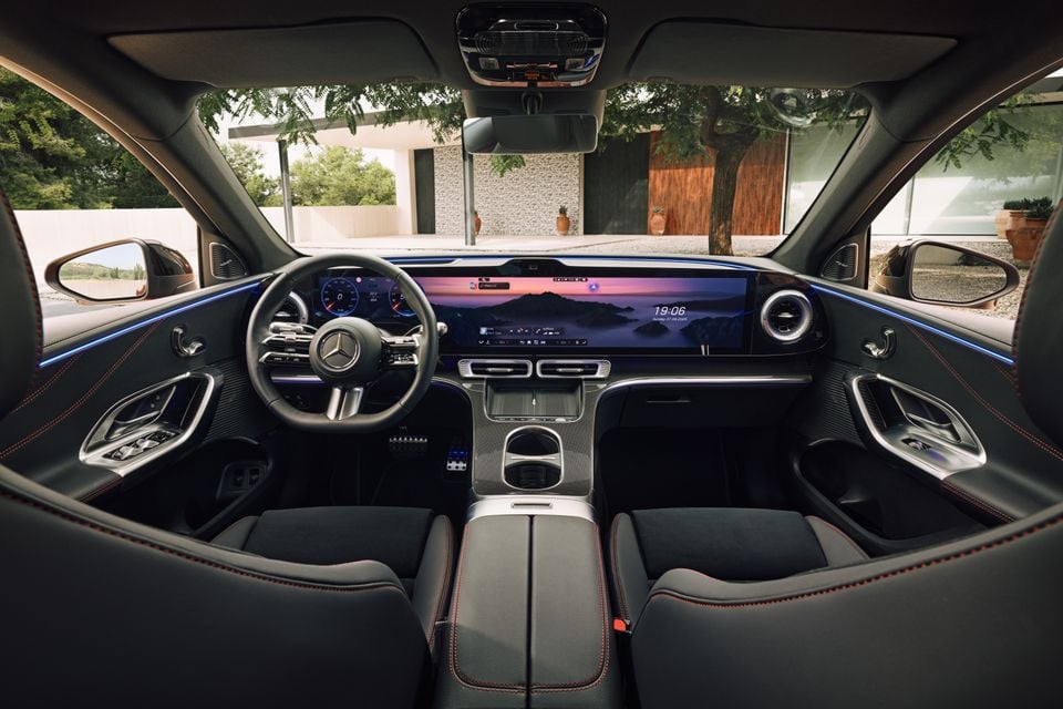 Interior of a Mercedes-Benz GLC400 Electric showing the wide curved digital display, Mercedes-Benz steering wheel, dark leather seats with red stitching, and ambient lighting across the dashboard