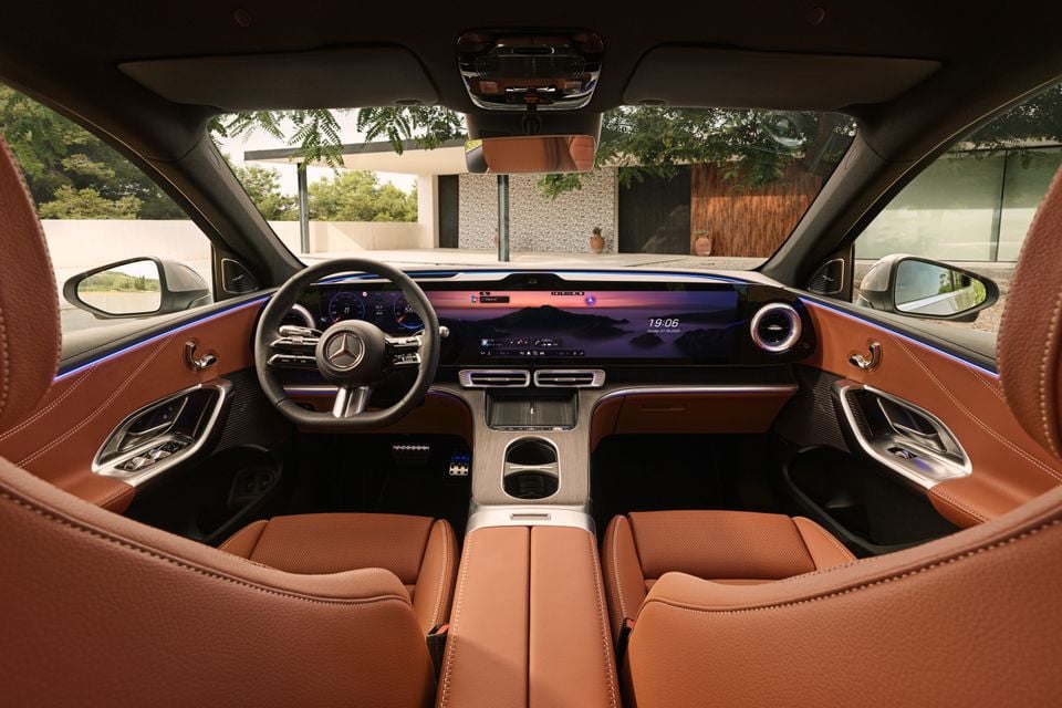 Interior of a 2027 Mercedes-Benz GLC 400 Electric showing the wide curved display screen, brown leather seats, and steering wheel with Mercedes-Benz logo