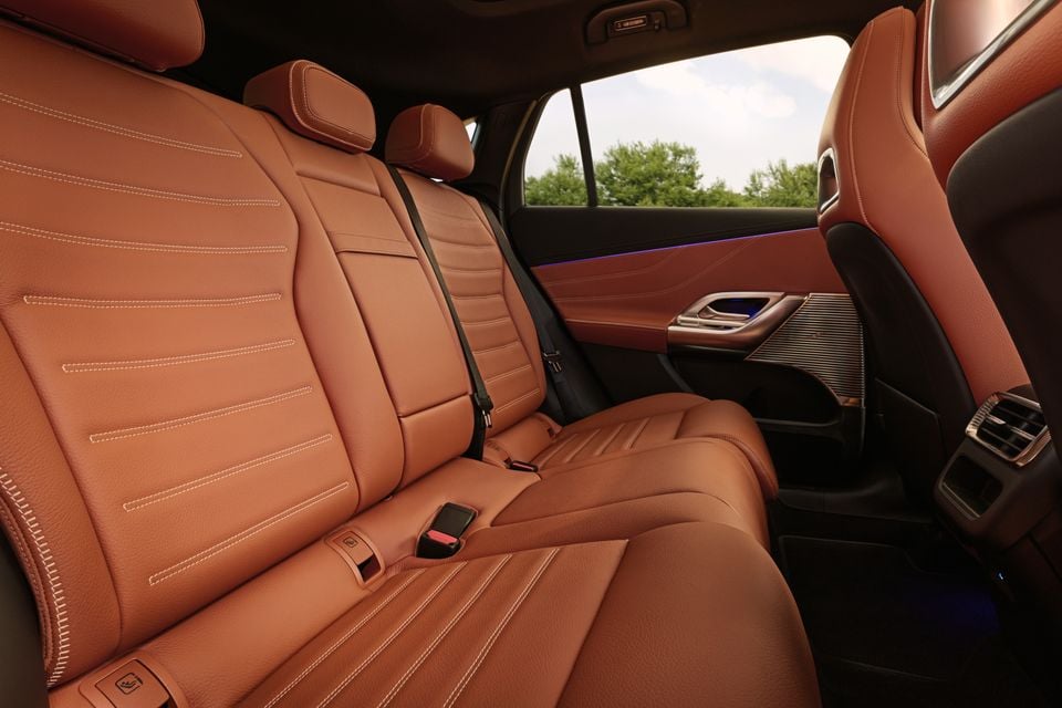 Tan leather rear seats of a 2027 Mercedes-Benz GLC400 Electric, showing stitched upholstery, door trim with ambient lighting, and a speaker grille