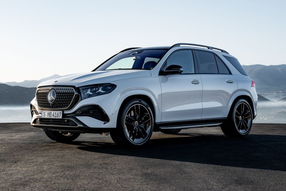 A white 2027 Mercedes-Benz GLE SUV seen from the front-side angle, parked on a hilltop with a misty mountain backdrop.