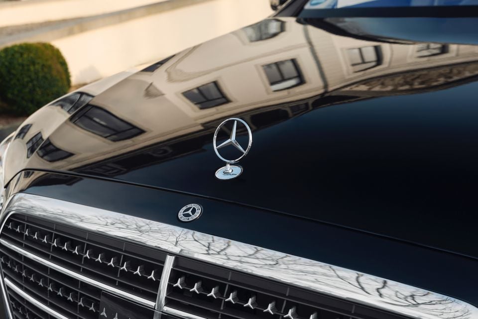 Close-up of the Mercedes-Benz star hood ornament and badge on the bonnet of a dark blue 2027 Mercedes-Benz S-Class sedan.