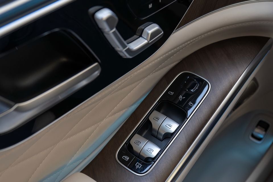 Close-up of the door panel controls and window switches in a Mercedes-Benz S-Class, showing brushed metal buttons and wood trim.