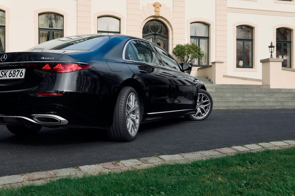 A black Mercedes-Benz S-Class sedan with 4Matic badging parked in a driveway outside a grand building, seen from the rear quarter