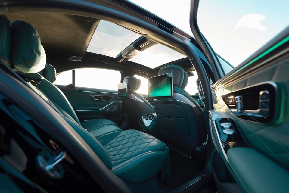 The rear seats of a Mercedes-Benz S-Class show teal leather upholstery, a large panoramic sunroof, and rear-seat entertainment screens.