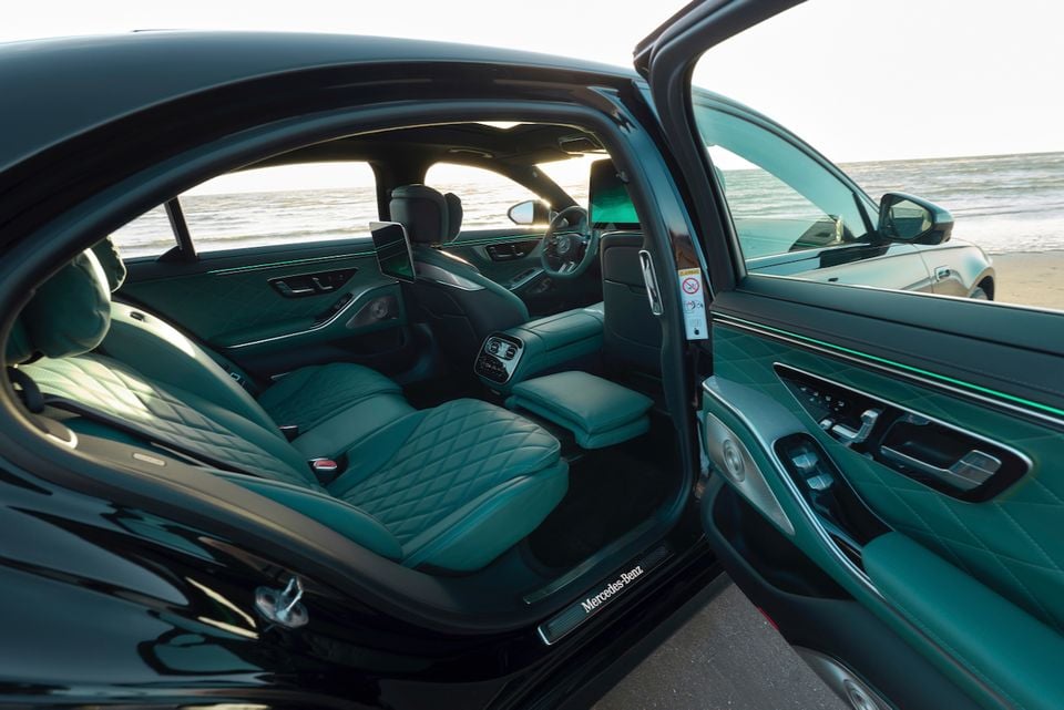 The rear seats of a Mercedes-Benz S-Class, upholstered in teal leather, seen through the open door with a beach in the background
