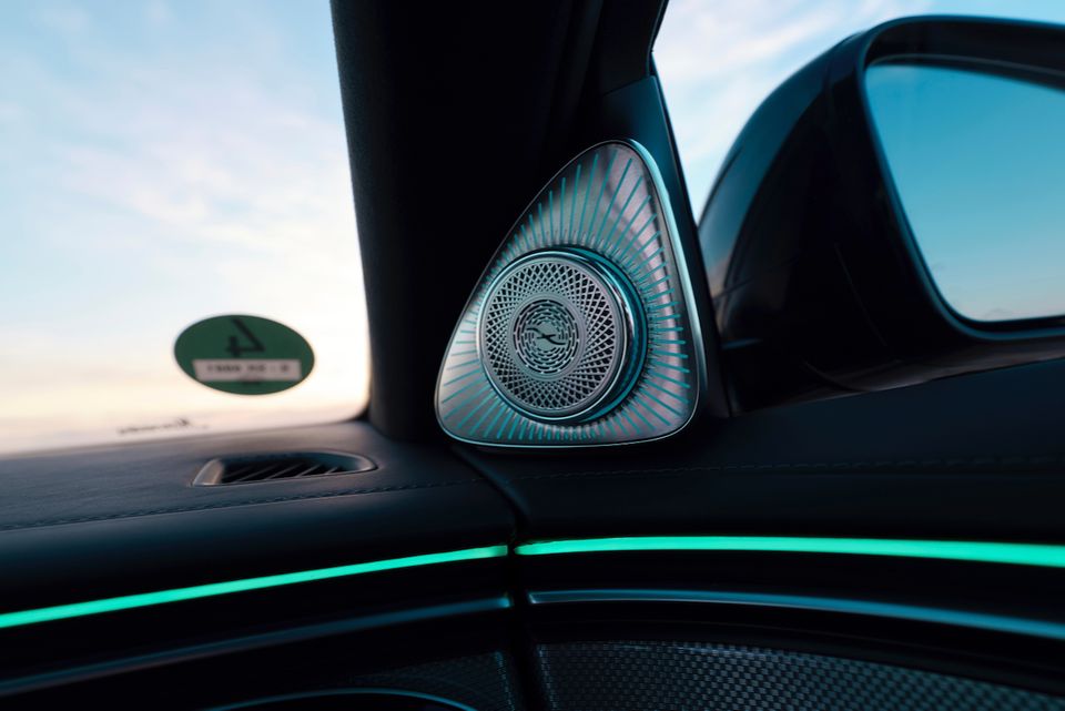 Close-up of a premium speaker on the interior door pillar of a Mercedes-Benz S-Class, with ambient teal lighting along the dashboard