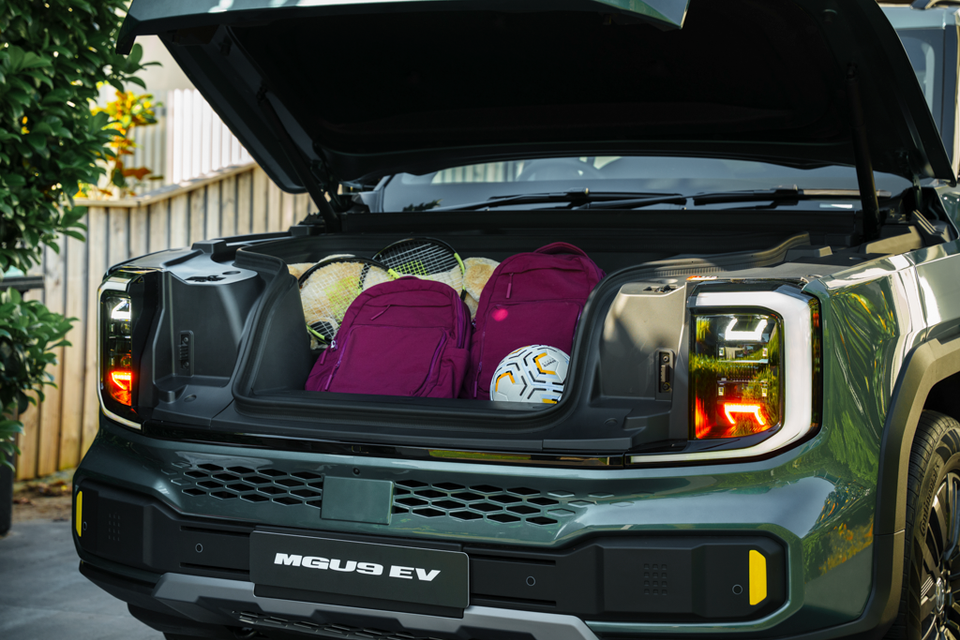 A green 2027 MG U9 EV ute with its front bonnet raised, showing a frunk holding two backpacks, tennis racquets and a soccer ball