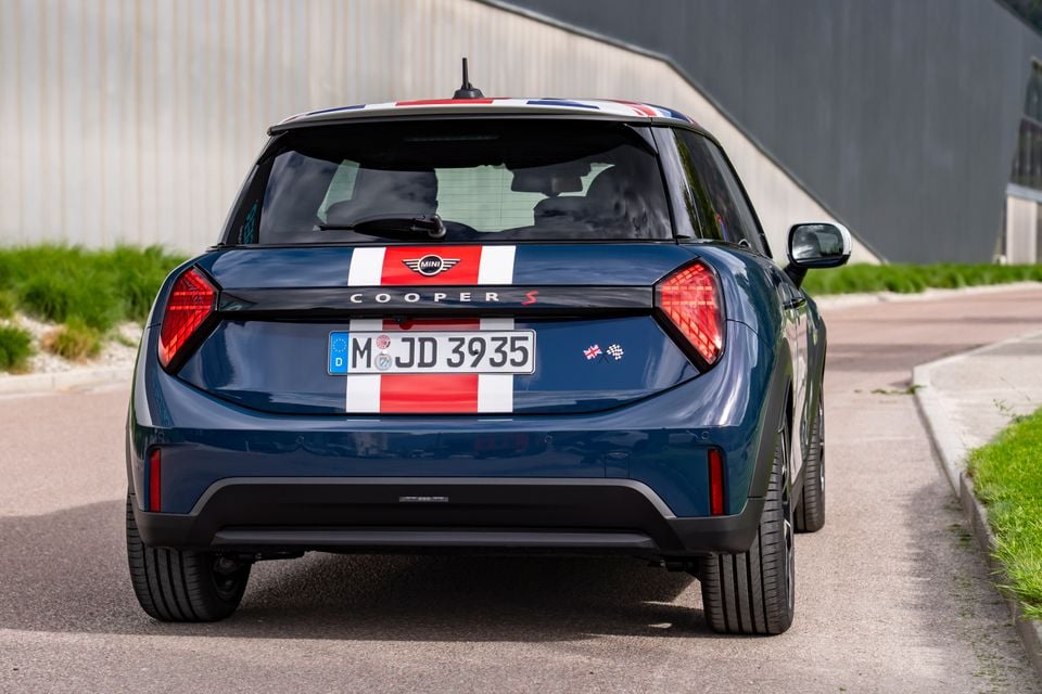 Rear view of a blue Mini Cooper S hatchback with Union Jack roof and red and white racing stripes, parked on a road
