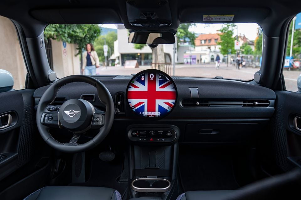 Interior of a Mini Cooper showing the dashboard, steering wheel, and circular central infotainment screen displaying a Union Jack design