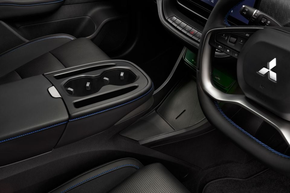 Close-up view of the centre console and steering wheel inside a Mitsubishi ASX, with blue contrast stitching and cup holders visible.