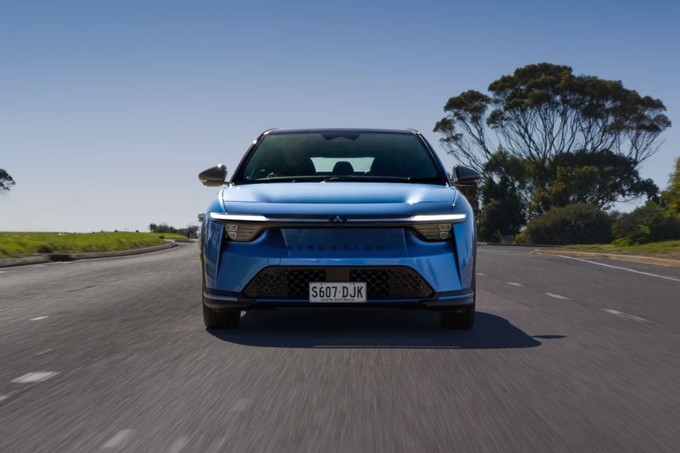 A blue 2027 Mitsubishi ASX small SUV driving on a road, seen head-on from the front.