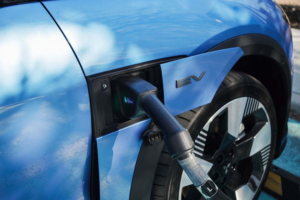 Close-up of a charging cable plugged into the port on a blue electric vehicle, with an "EV" badge visible on the charging flap.