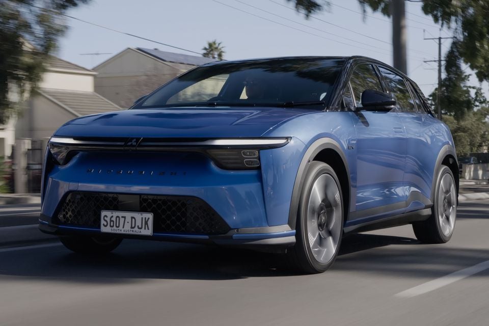 A blue 2027 Mitsubishi ASX electric SUV driving on a suburban street, seen from the front quarter view