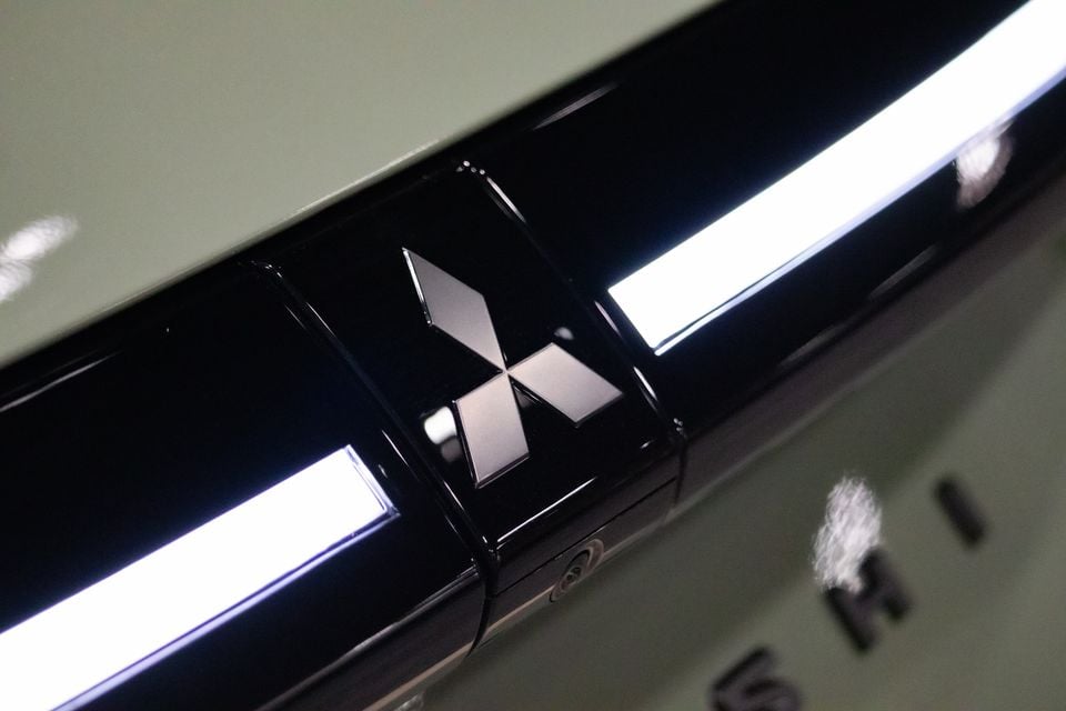 Close do emblema da Mitsubishi em um painel preto brilhante entre barras de luz iluminadas em um Mitsubishi ASX VR-E 2027 verde